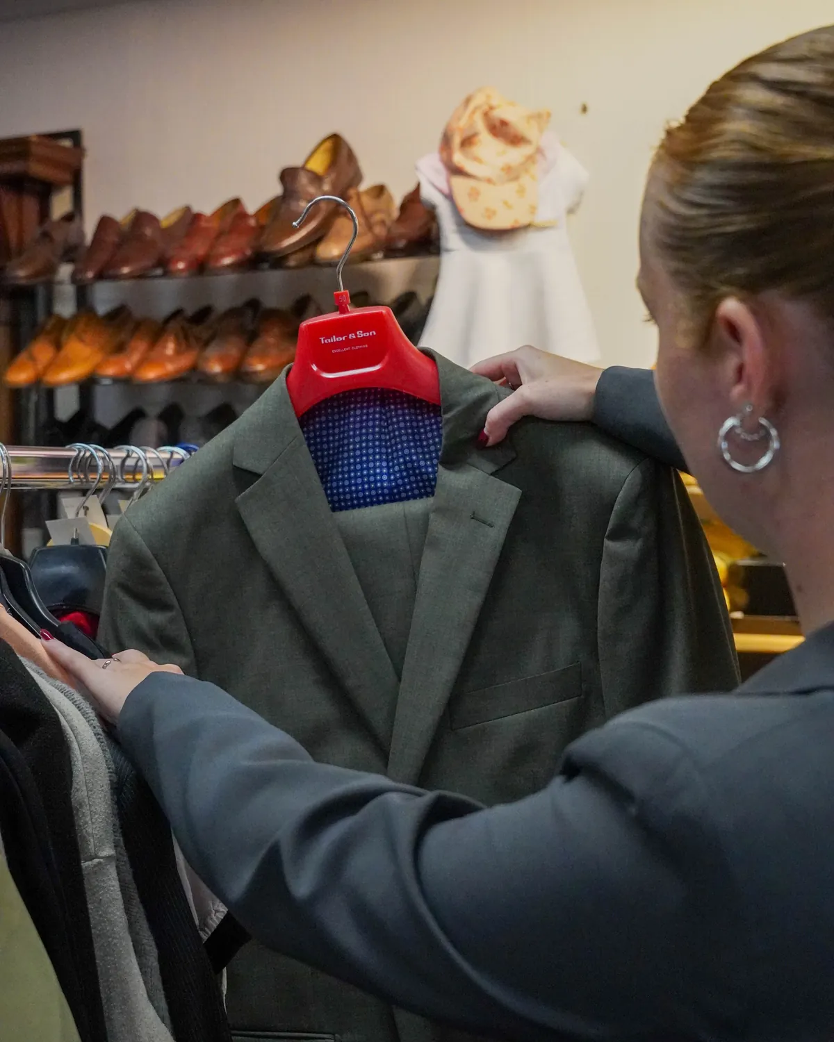 Een klant houdt een grijs colbert omhoog bij het kledingrek, met schoenen op de achtergrond